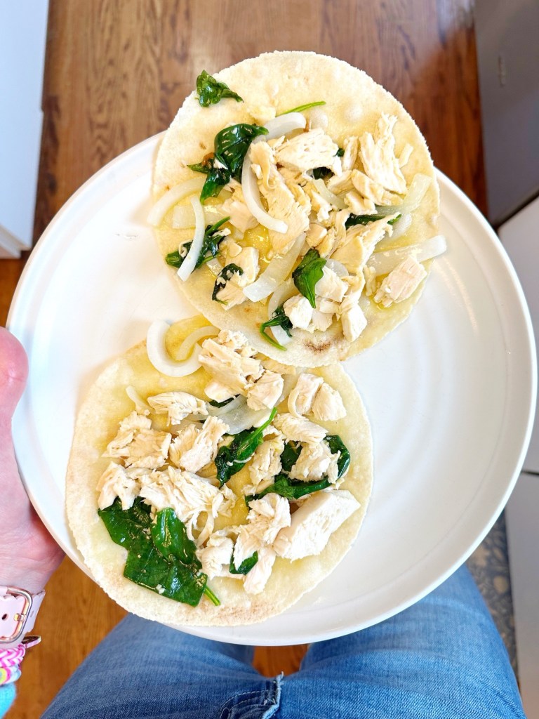 image is of a homemade pizza with almond flour crust, rotisserie chicken, spinach, olive oil, garlic and onion